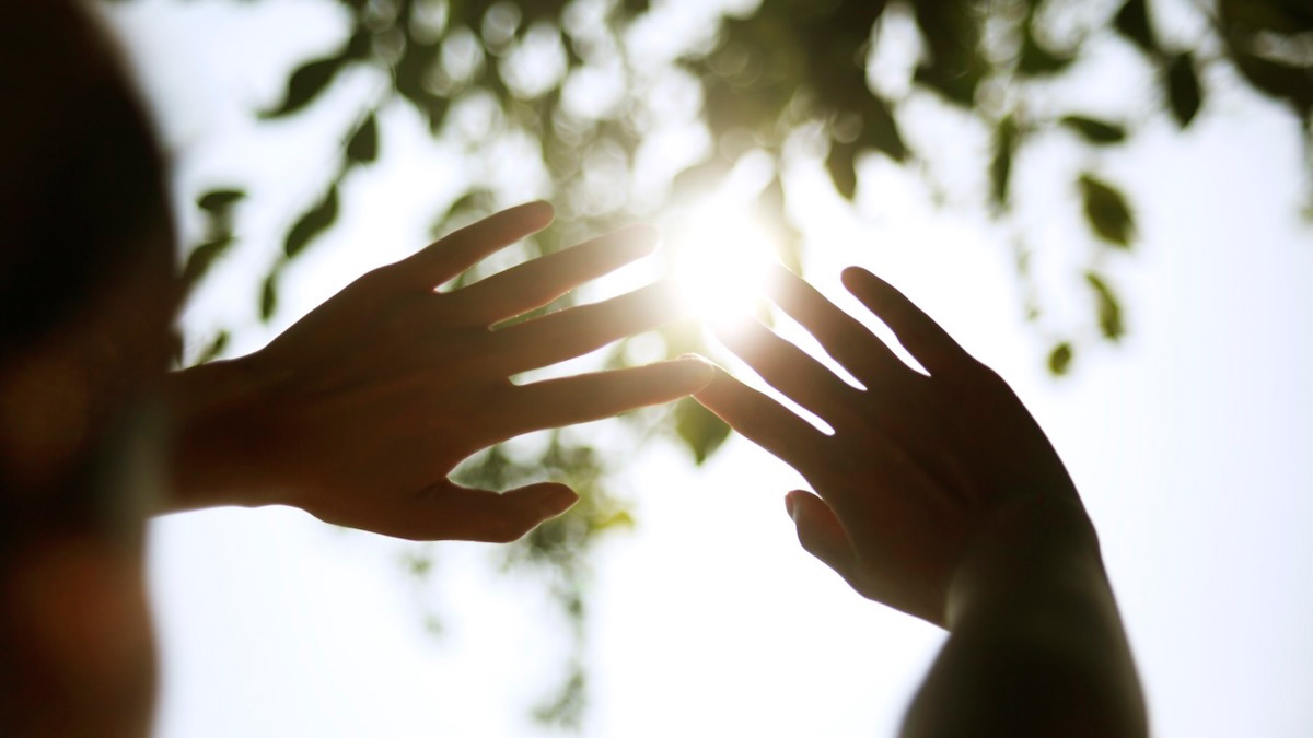 two hands raised up to the sky with the sunlight coming through