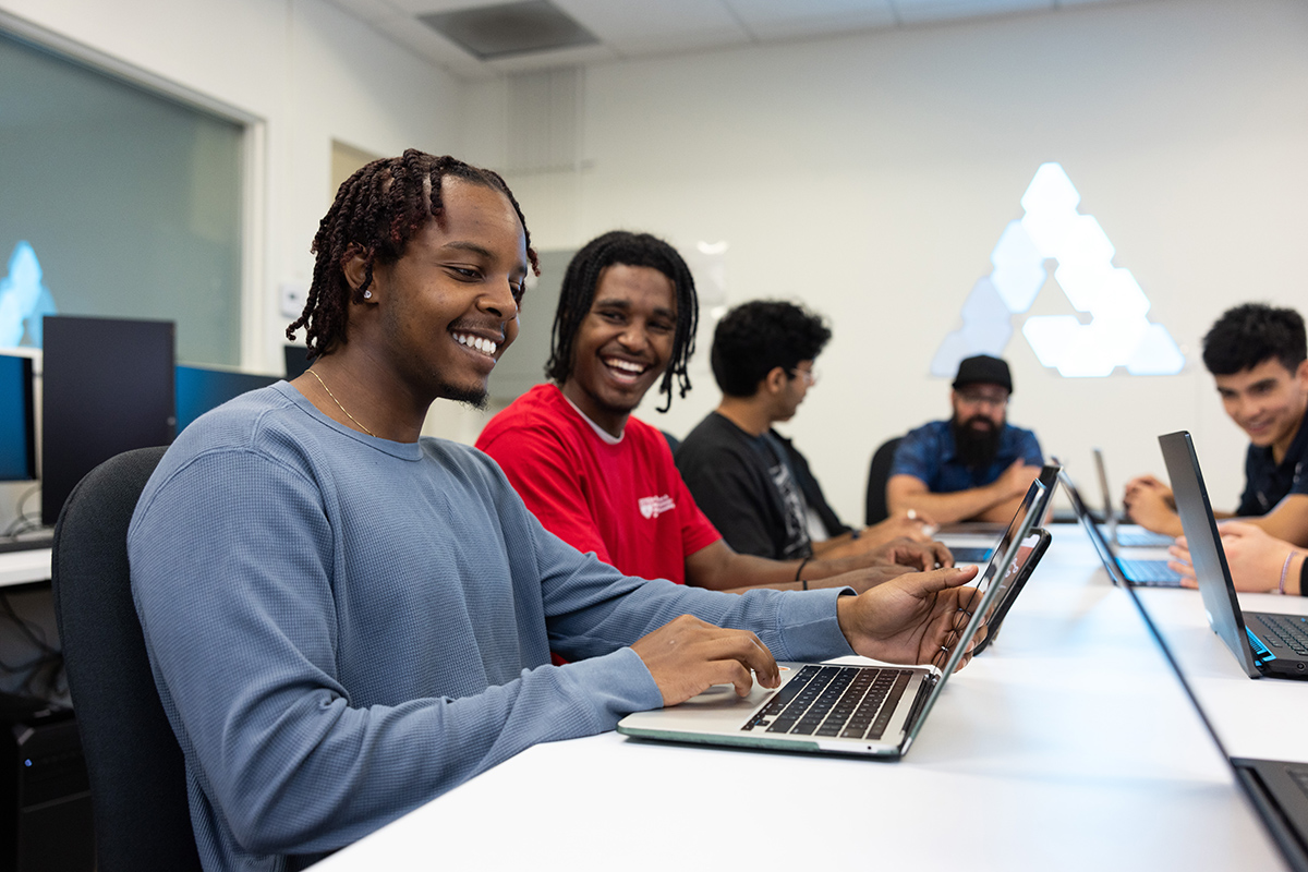 Three students on laptops smiling at each other