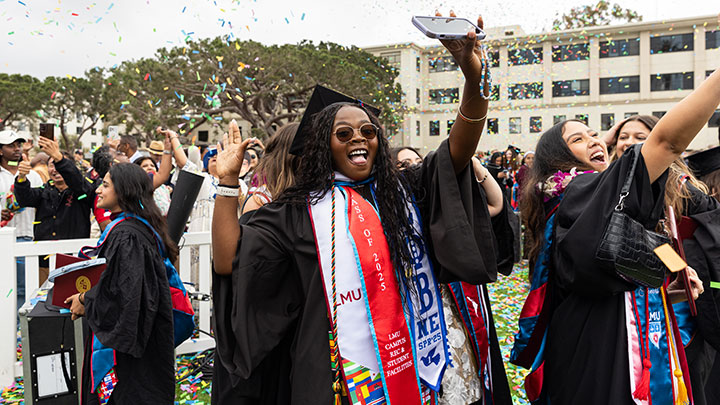 A student raising their hands triumphantly upon the completion of commencement with confetti in the air around them