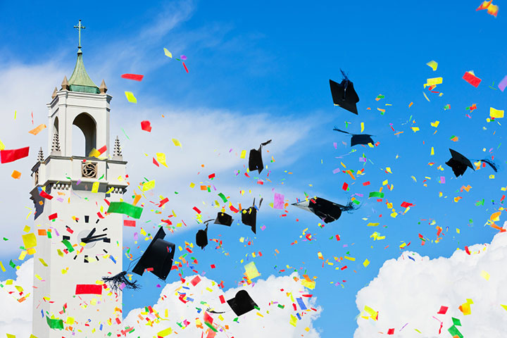 Confetti and graduation caps being thrown into the air, with a clear sky and Sacred Heart Chapel Clock Tower visible in the distance