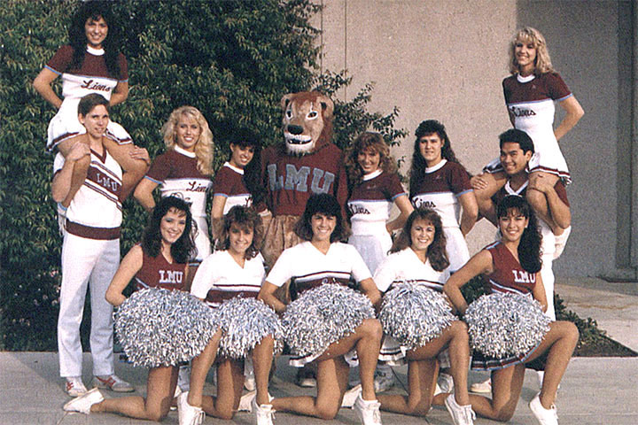 A photo of the pep squad posing in a group outside of Gersten with Iggy standing in the middle wearing an LMU branded sweater