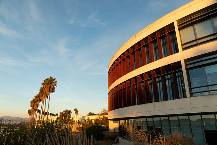The William H Hannon Library at sunset with a view of palm trees along the bluff and Los Angeles in the distance